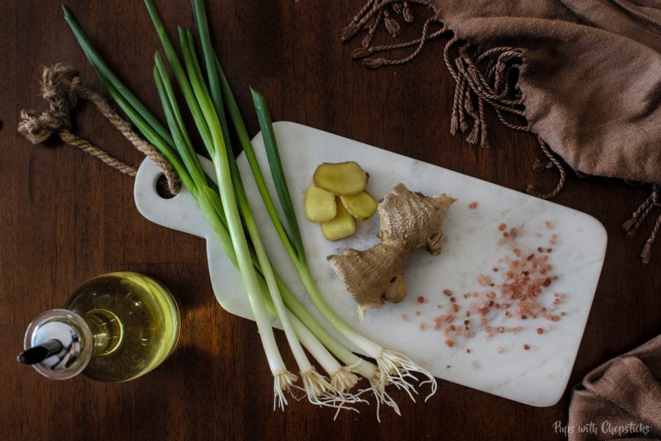 Green onions, oil, ginger and salt laid out on a cutting board on a table.