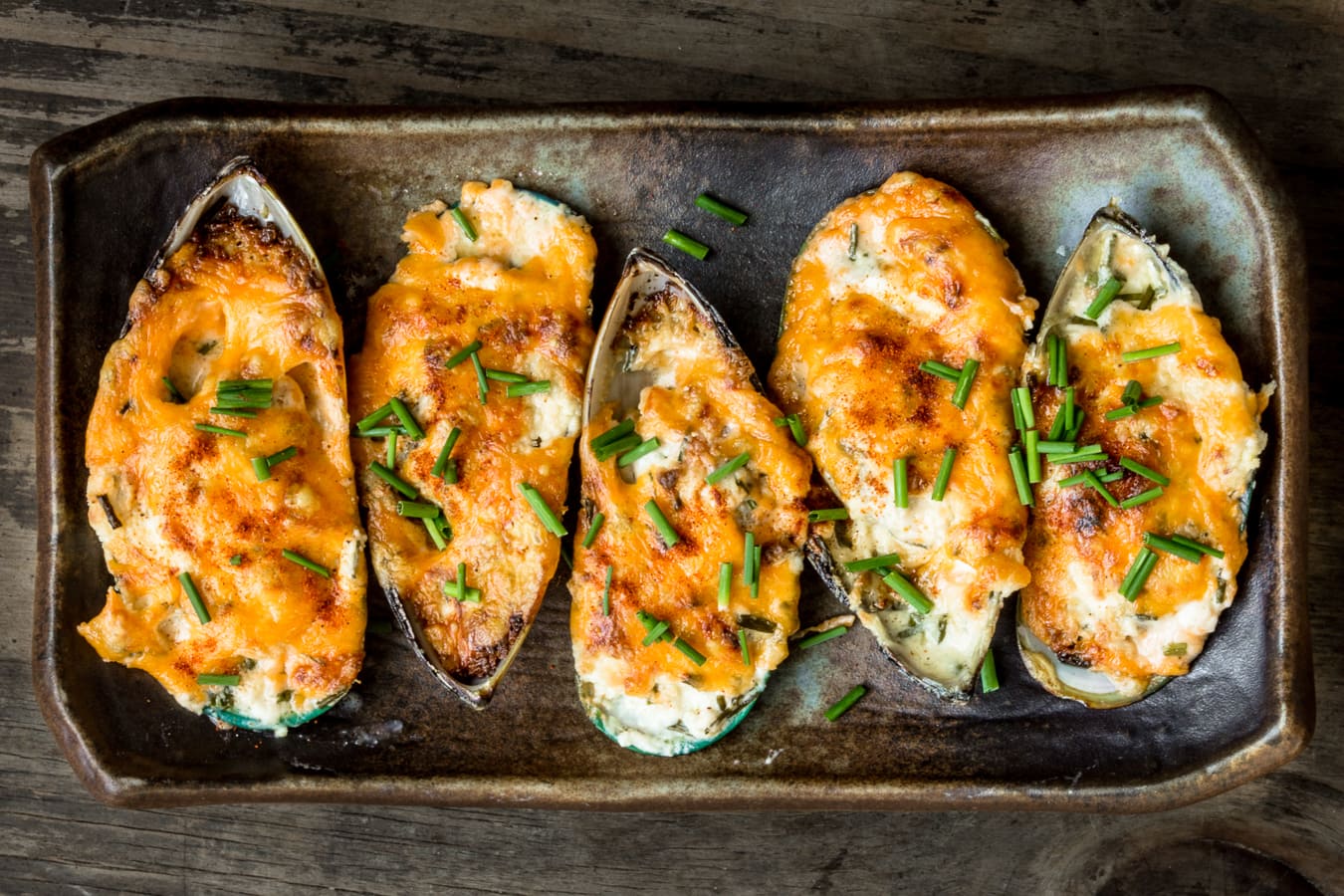 Garlic cheese mussels served on a brown plate and topped with freshly cut chives