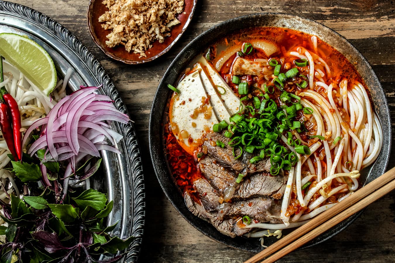 A large bowl of bun bo hue on a wooden table