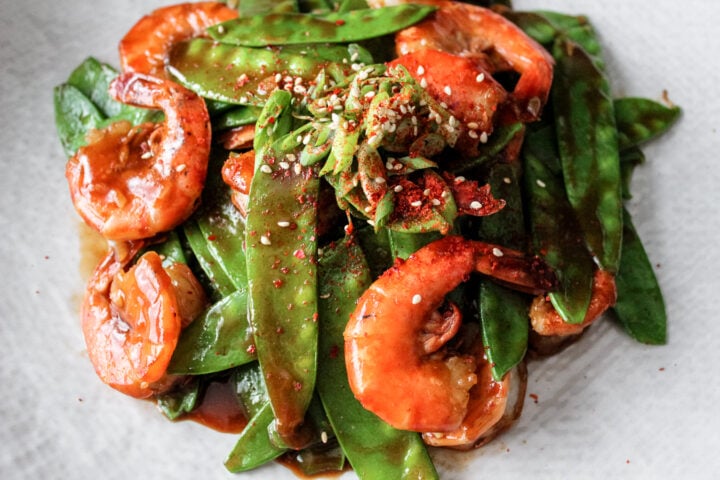 spicy shrimp and snow peas on a white plate.