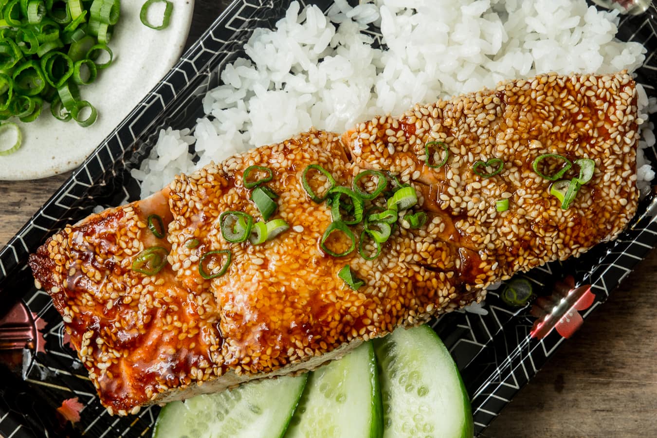 Teriyaki salmon fish served with rice and a side of cucumbers