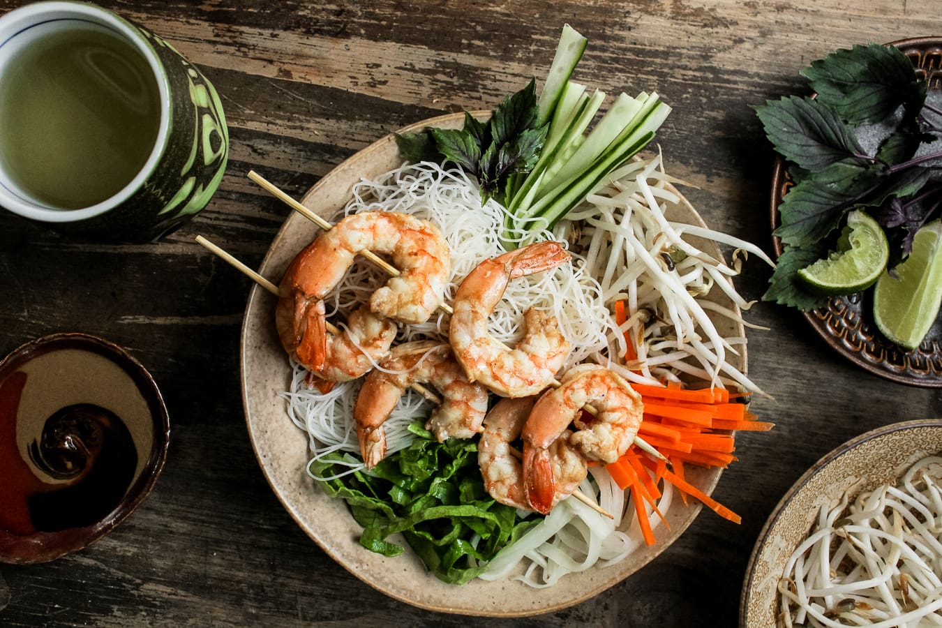 A bowl of vermicelli with Vietnamese grilled shrimp on top served with a side of tea