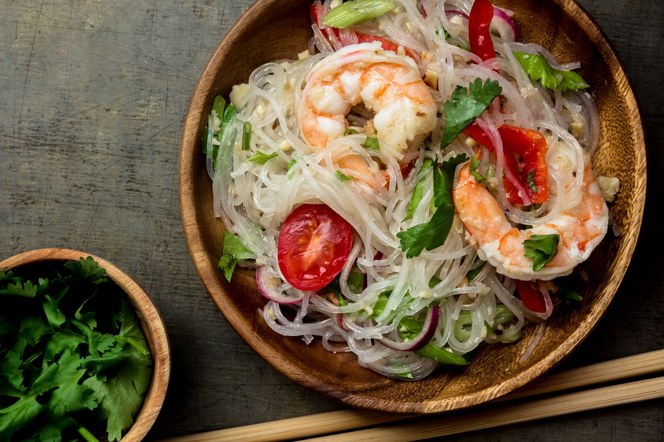 Thai glass noodle salad (Yum Woon Sen) with large shrimp served on a wooden plate on a metal table.