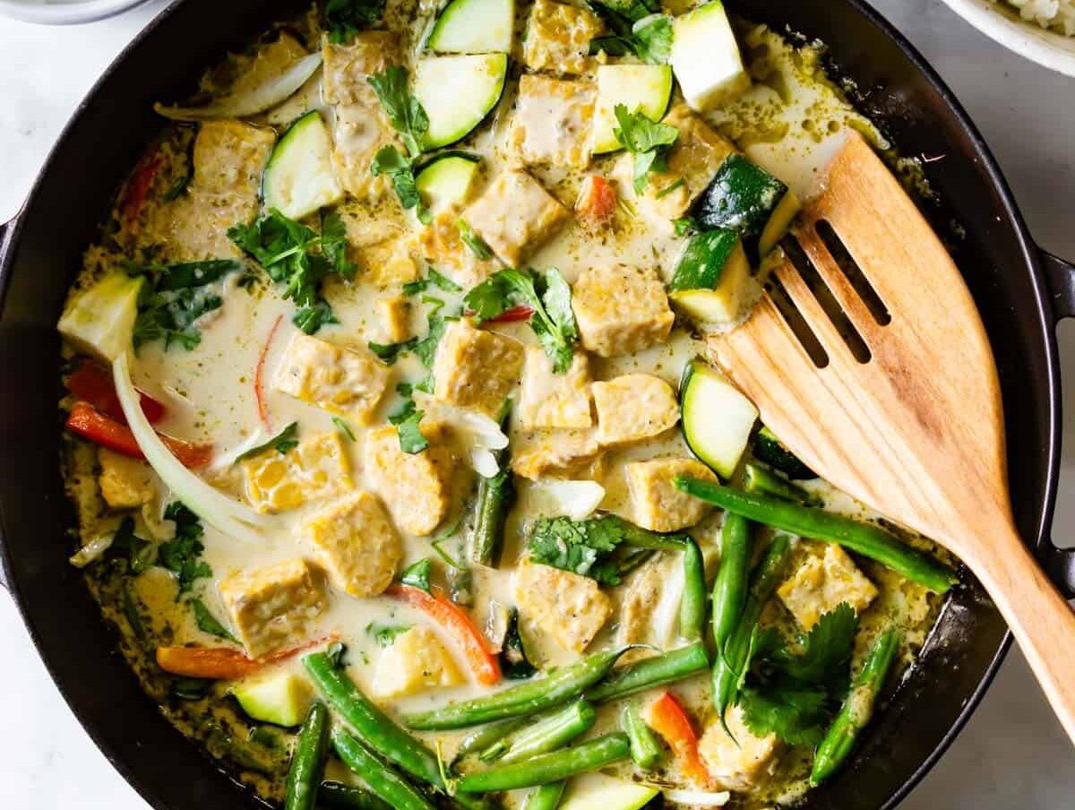 tempeh green curry in a frying pan with a wooden spoon.