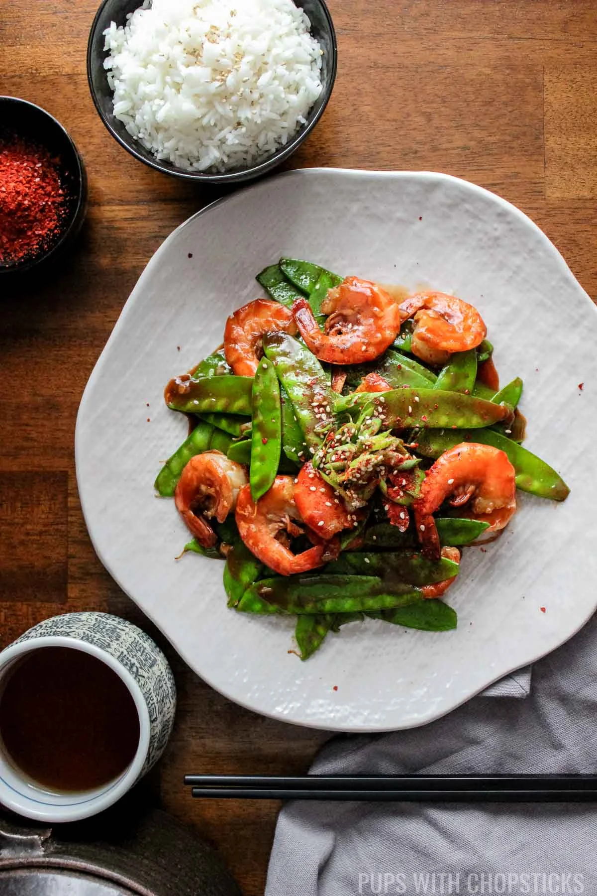 Spicy Garlic Shrimp with Snow Peas on a plate with a side of rice and a cup of tea on a table