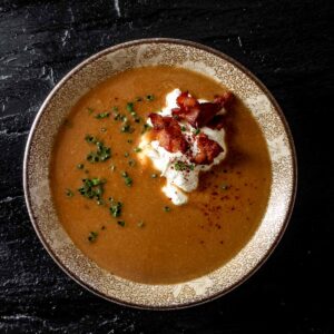 A small bowl of miso pumpkin soup garnished with bacon and sour cream