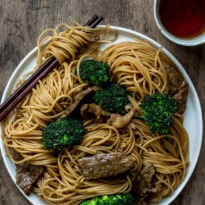 A plate of beef and broccoli noodle stir fry served with a side of tea