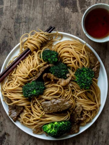 A plate of beef and broccoli noodle stir fry served with a side of tea