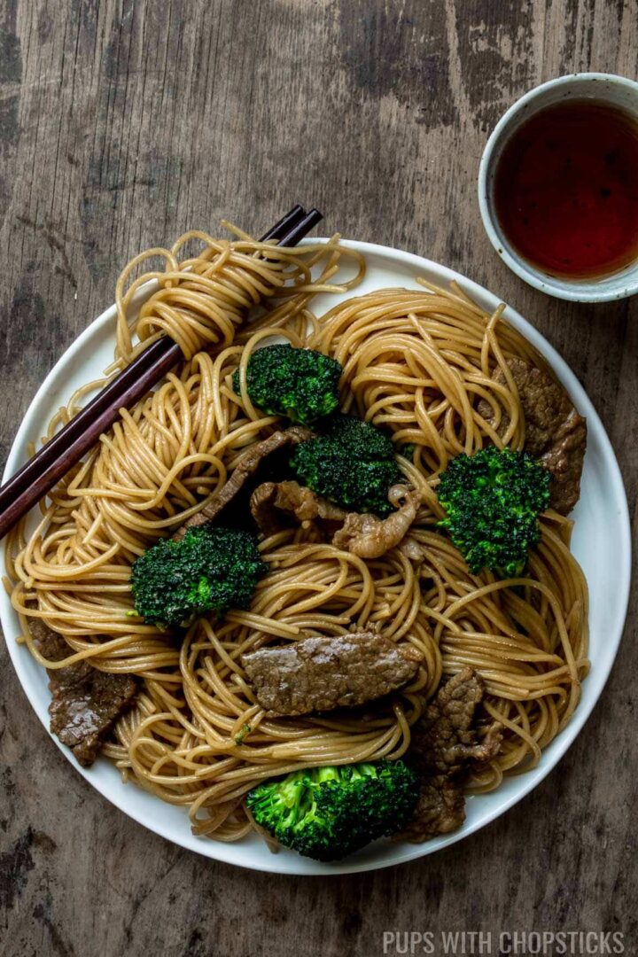 A plate of fried noodles with beef and broccoli served with tea
