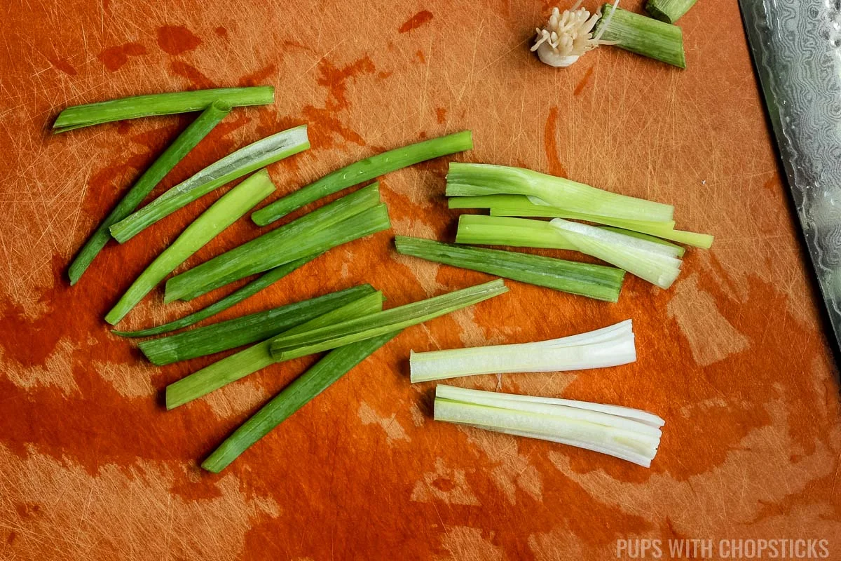 Green onions cut into 2 inch length pieces on a cutting board.
