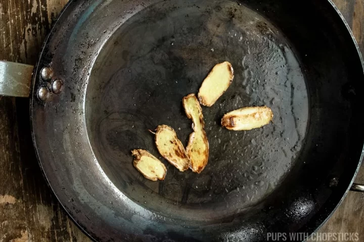 Ginger slices being toasted in oil in a frying pan.
