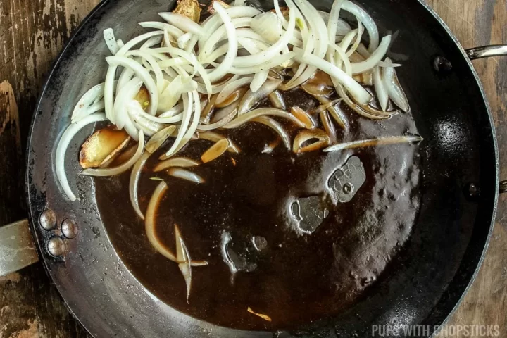 A frying pan with stir fried onions, and stir fry sauce.