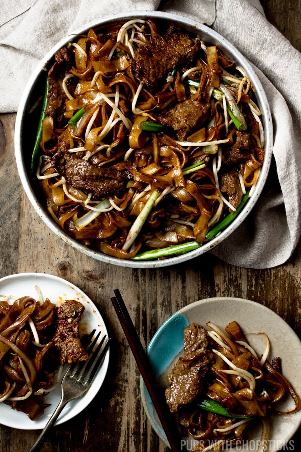 Beef Chow Fun (Beef Ho Fun) in a metal bowl with 2 plates of it being served and eaten