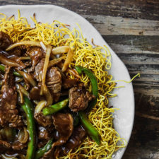 A plate of Cantonese beef chow mein with beef and veg on top of crispy noodles