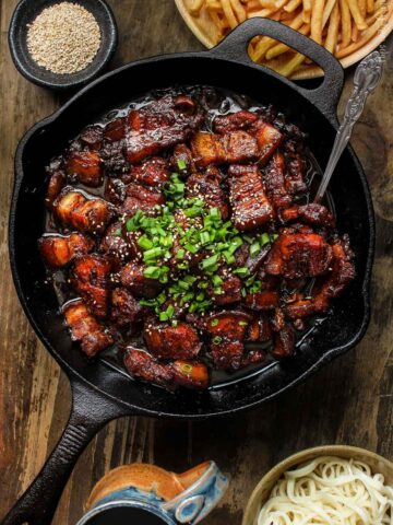 Chinese style beer braised pork belly in a cast iron pan served with fries and noodles
