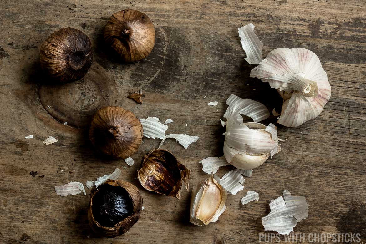 Black garlic and regular garlic laid out on a wooden table