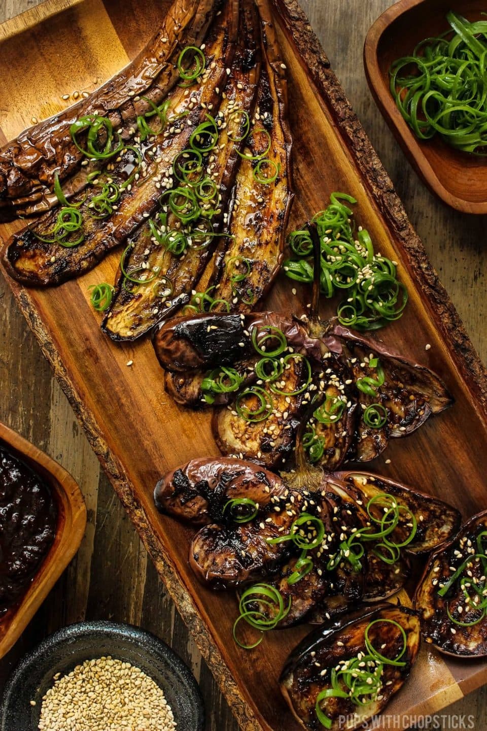 Miso eggplant fanned out on a wooden plate and served with sesame seeds and green onions