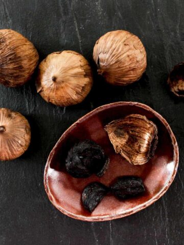 Whole bulbs of black garlic, and peeled cloves of black garlic on a plate