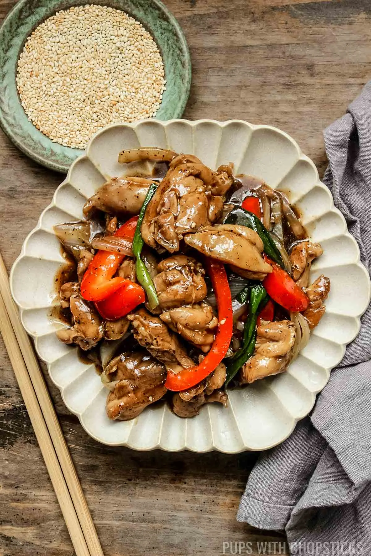 black pepper chicken stir fry on a white plate with sesame seeds on the side.