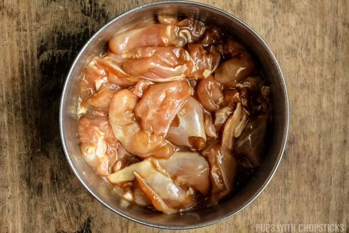 Chicken being marinated in a metal bowl.