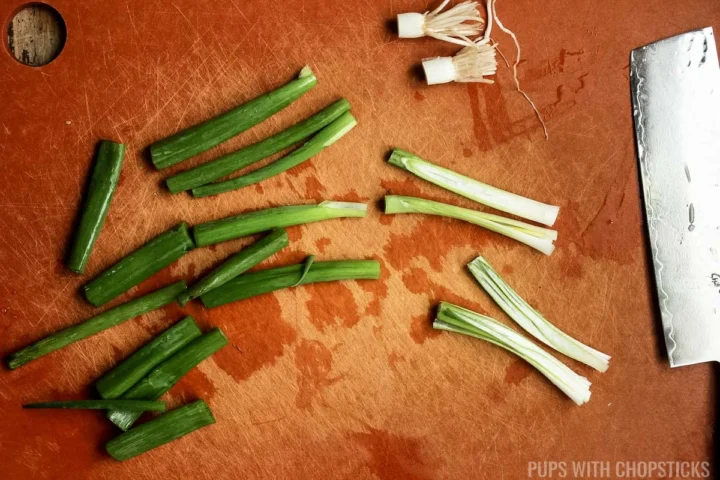 green onions chopped into 2 inch pieces on a cutting board.