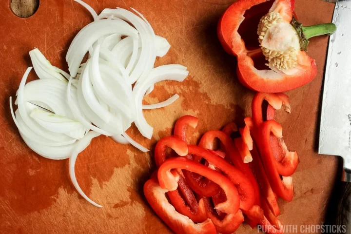 white onion and red pepper being cut on a cutting board.