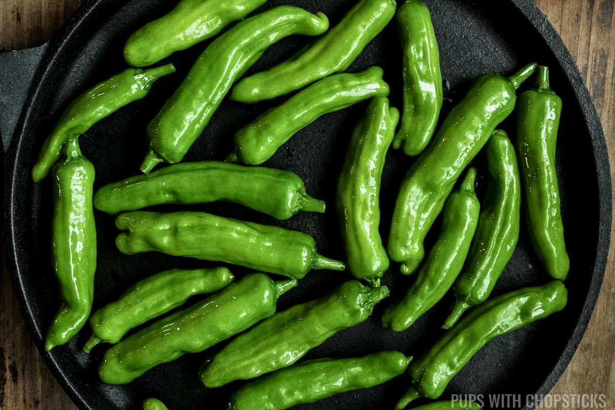 Add shishito peppers to hot cast iron pan