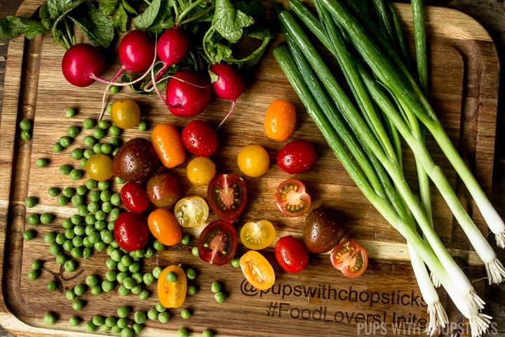Fresh local produce on a cutting board (fresh peas, radishes, baby tomatoes, green onions)