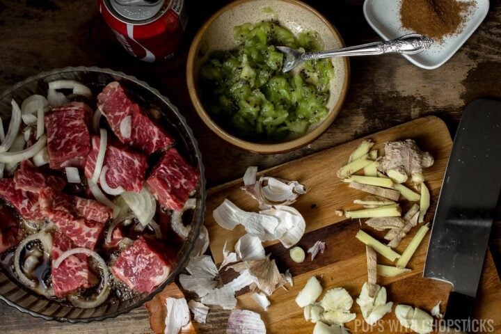 A large bowl of beef chunks being marinated with kiwi, coke onions, garlic and ginger to tenderize it.
