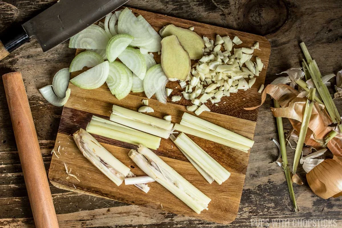 Sliced ginger, onions and minced garlic and smashed lemongrass being prepared on a cutting board for bo kho