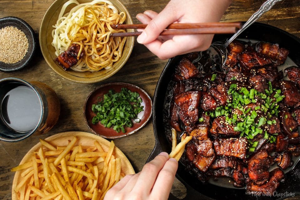 Chinese style beer braised pork belly being eaten with a bowl of noodles and a side of fries