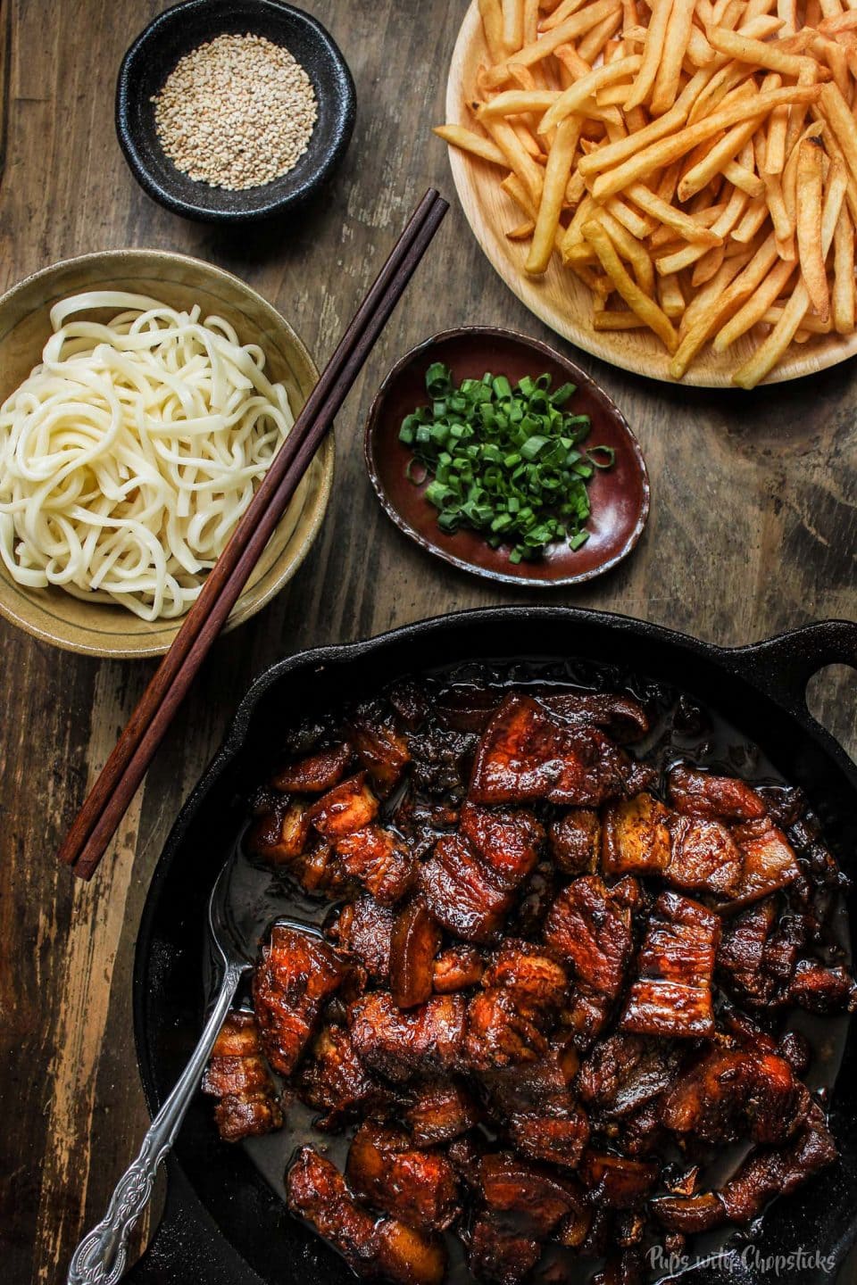 Chinese style beer braised pork belly in a cast iron pan served with fries and noodles