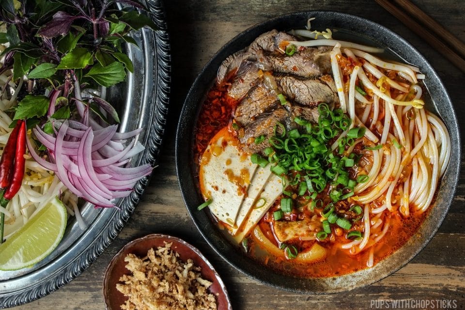 bun bo hue in a large black bowl with garnishes on the side