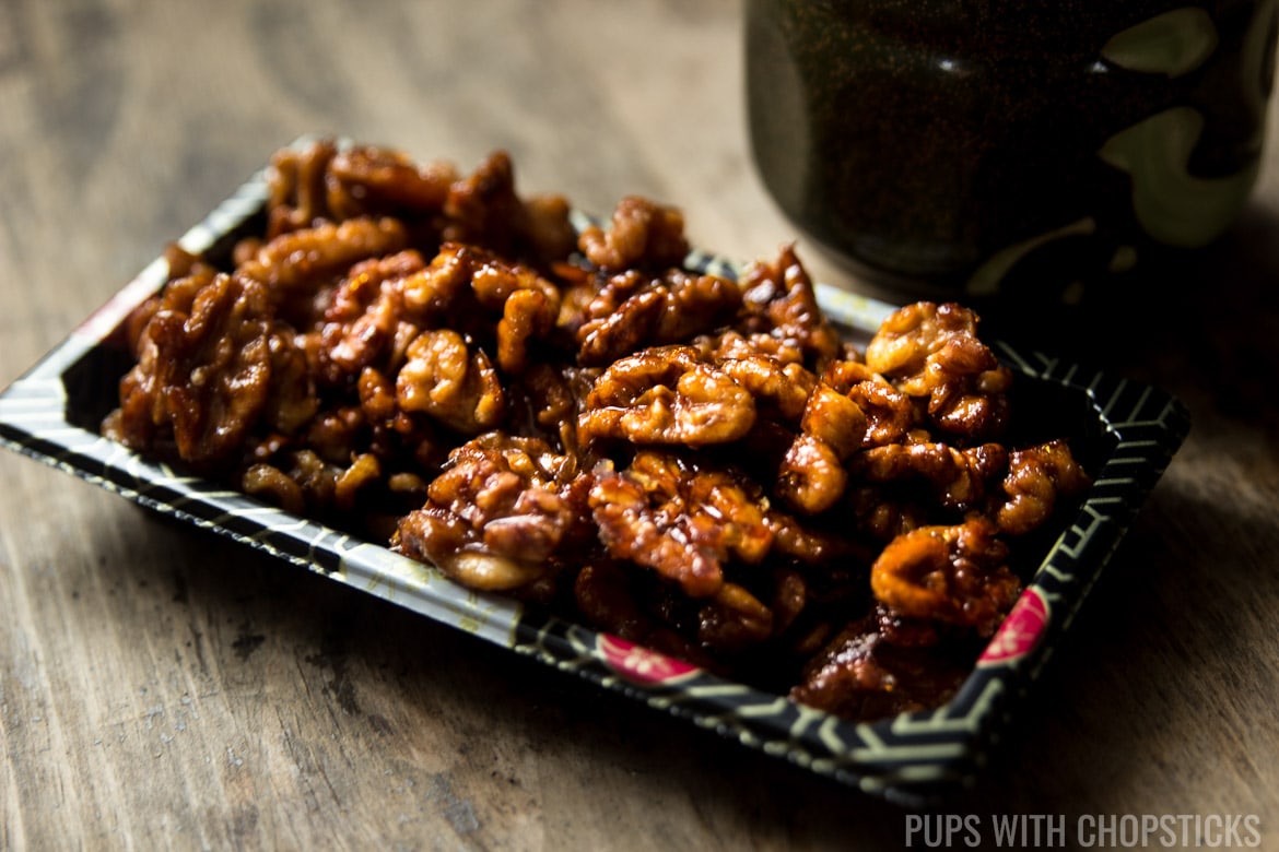 Side view of candied walnuts in a black gray with a cup of tea