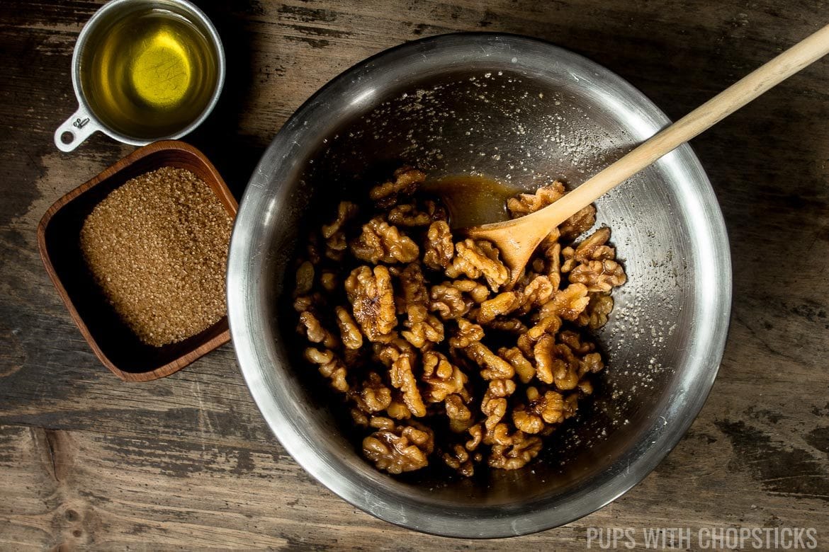 Freshly boiled and hot walnuts being mixed in a metal bowl with sugar and oil