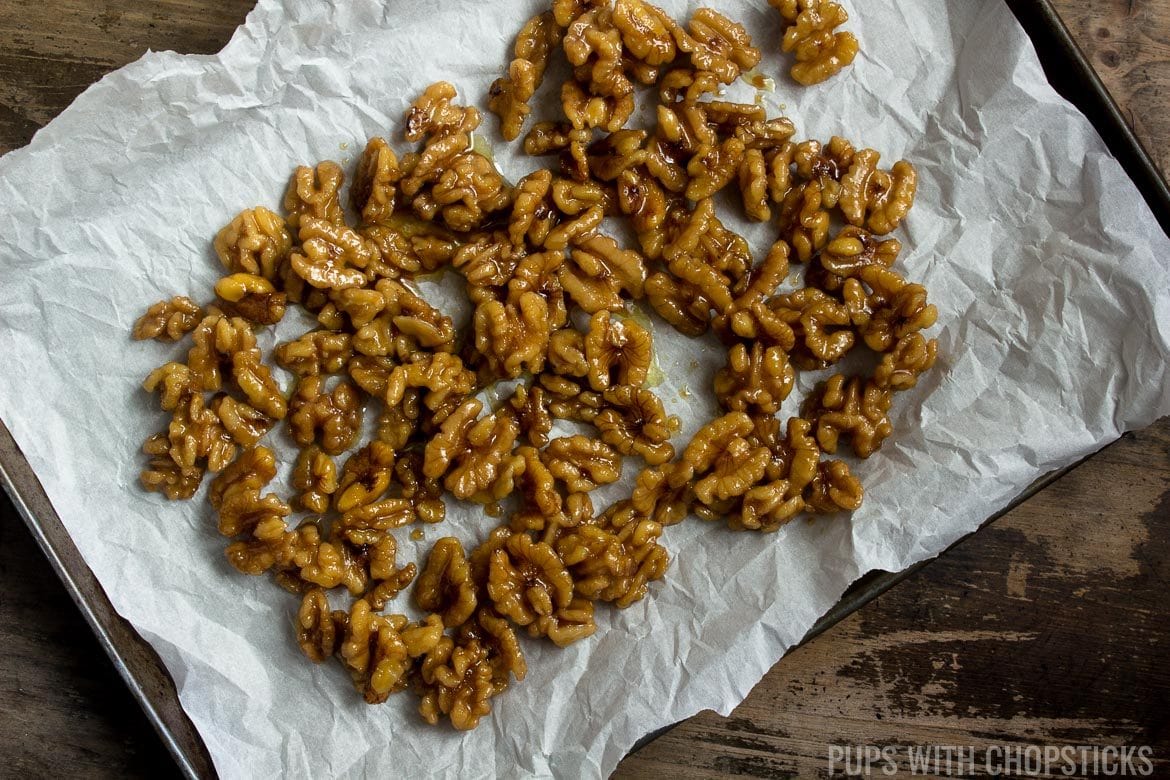 Walnuts coated in sugar and oil and laid out in a flat layer on parchment on a cookie sheet for the oven