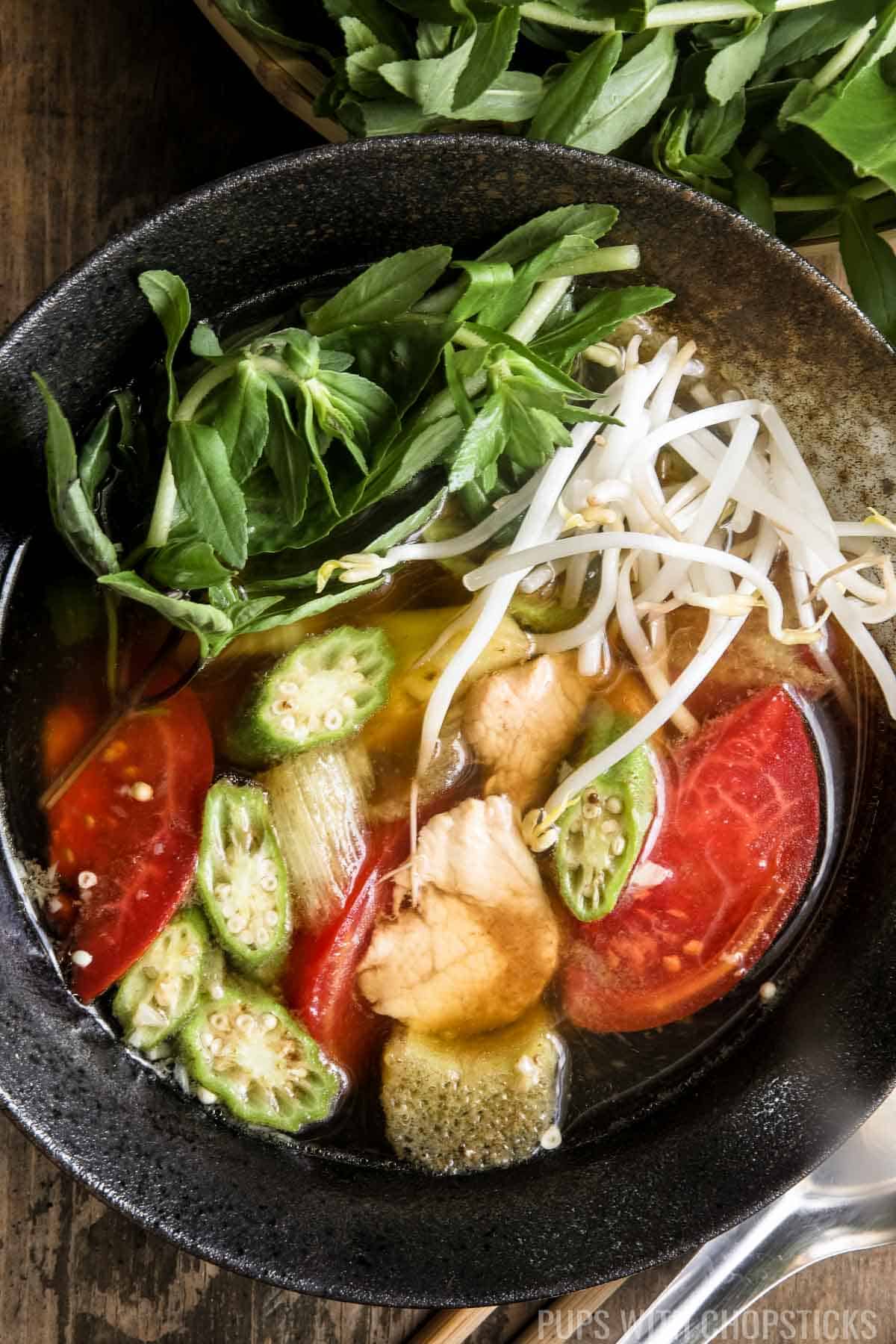 Close up of canh chua (Vietnamese sour soup) made with pineapples and tomatoes in a black bowl