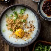 A close up of chicken congee in a large black bowl with a egg.