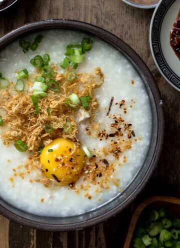 A close up of chicken congee in a large black bowl with a egg.