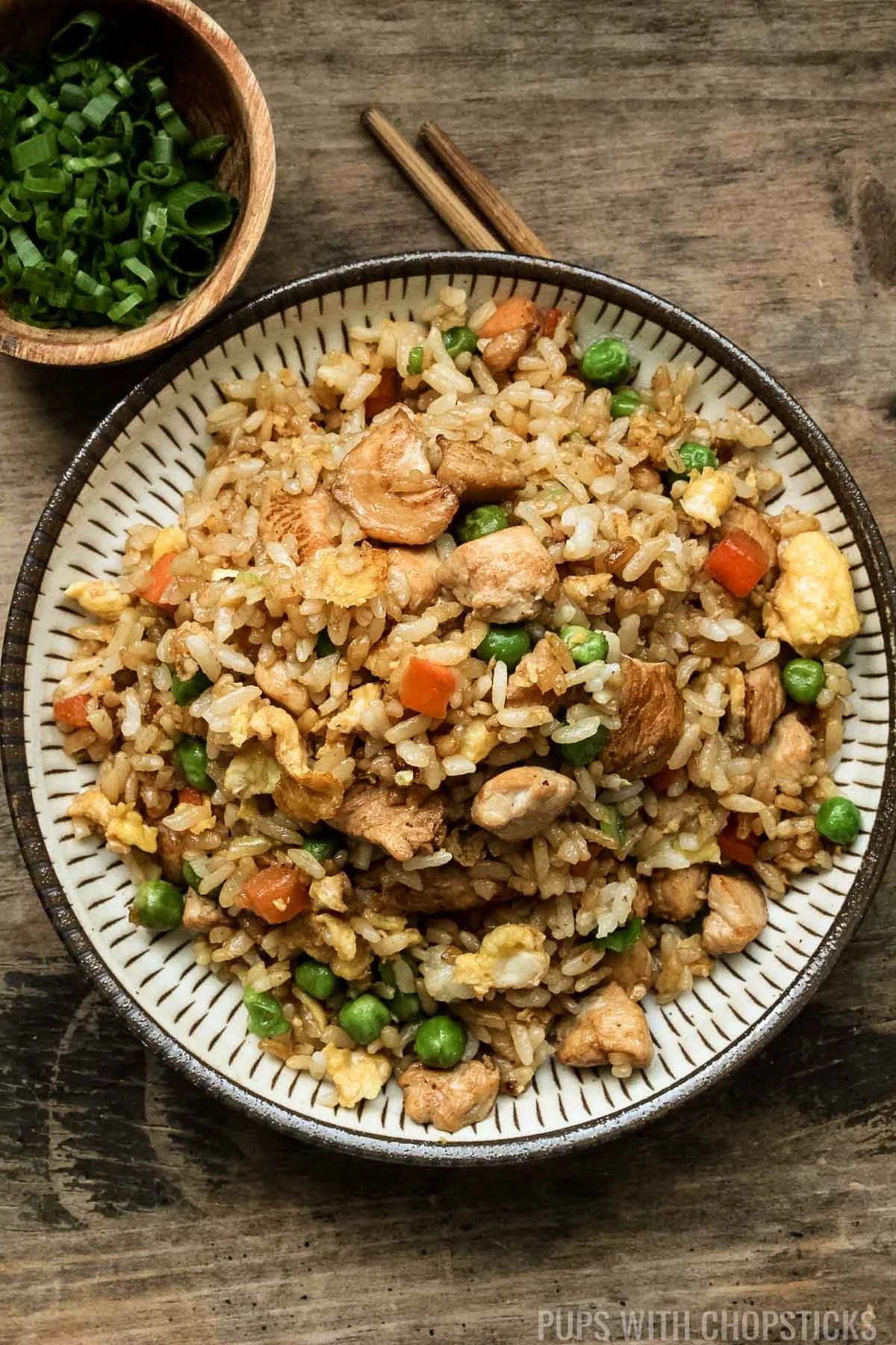 Chicken fried rice on a plate with chopsticks and green onions on the side.