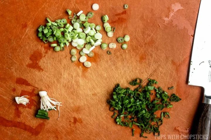 Chopping green onions on a cutting board, separating whites and green.