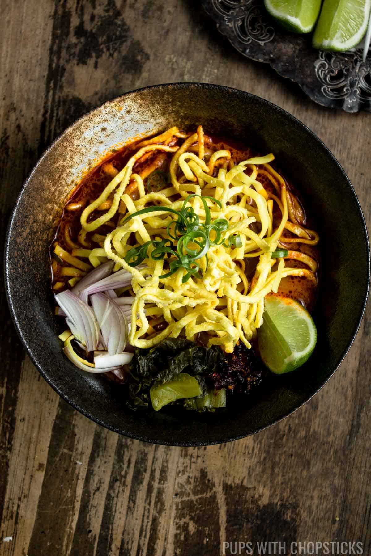A large bowl of Khao soi topped with crispy egg noodles with a thai curry noodle soup