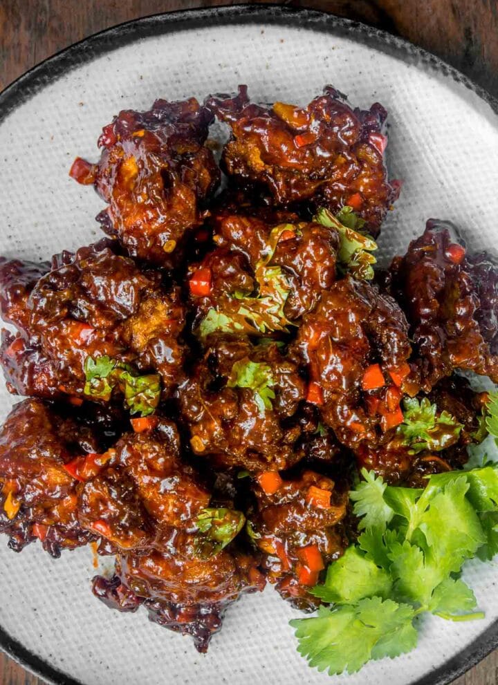 Chicken Manchurian on a blue plate on a wooden table with wooden chopsticks