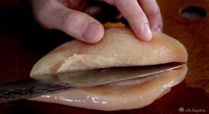 Butterflying a chicken breast from a side view with a knife.