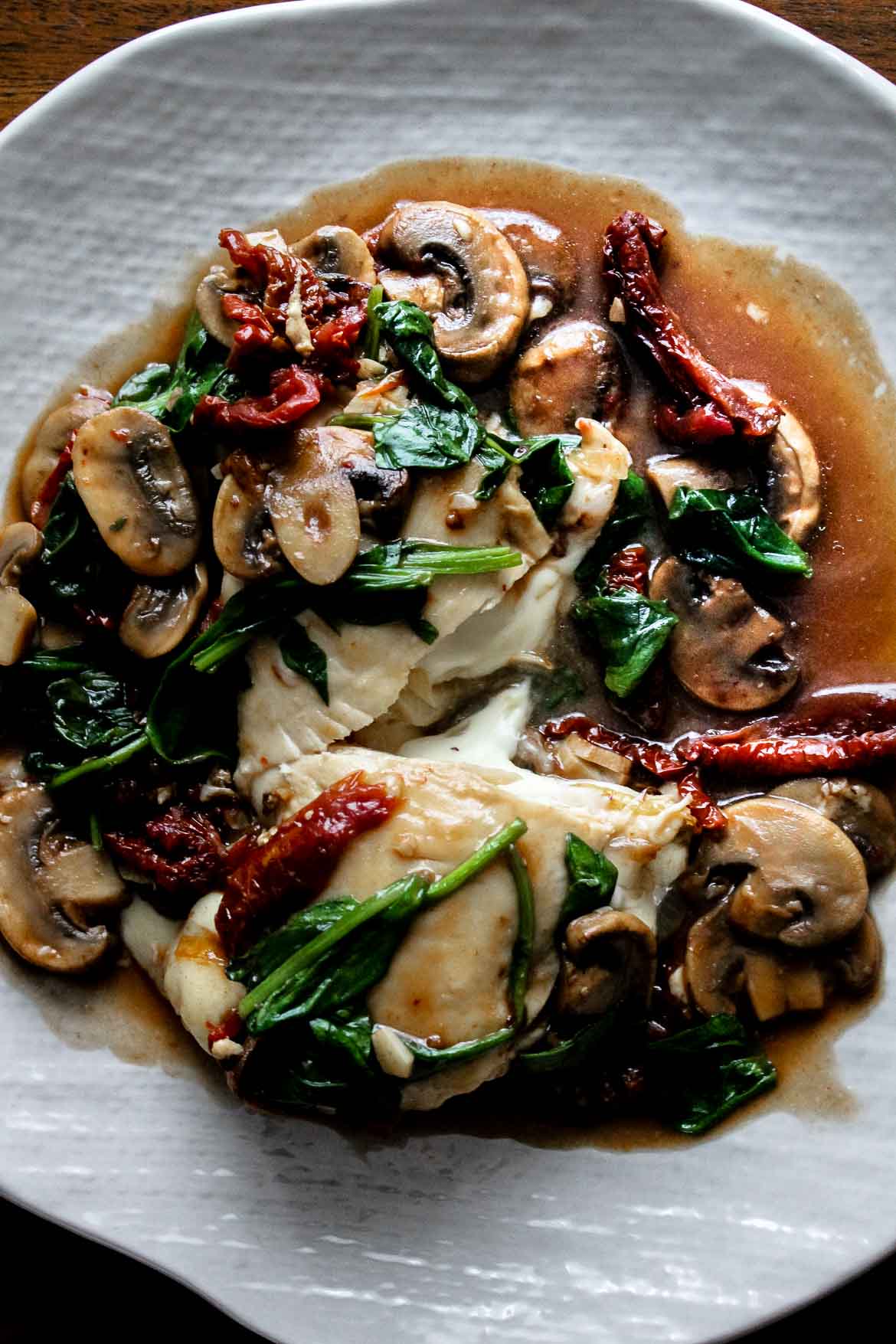Chicken Marsala stuffed with cheese and topped with spinach and sun dried tomatoes on a plate