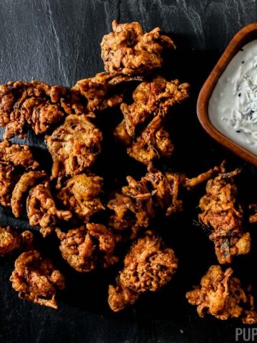 Chicken pakora laid out on a black plate with coconut dip on the side
