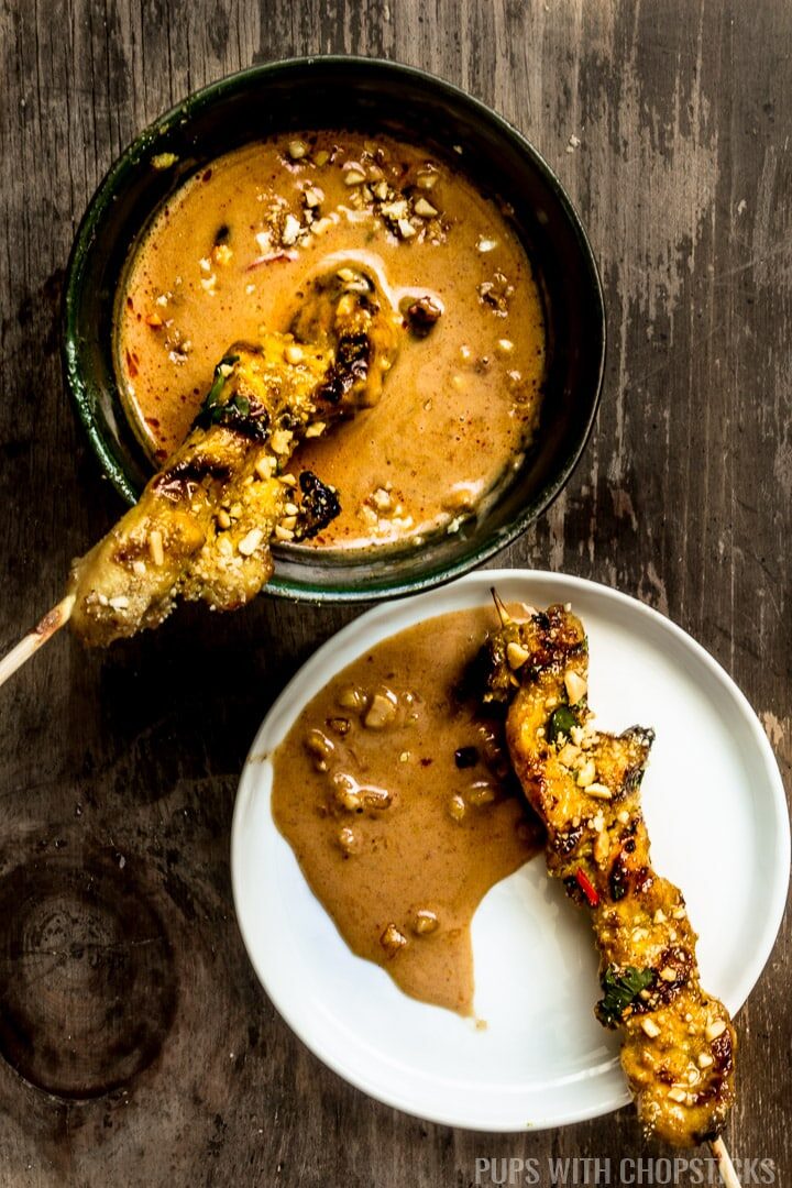 Two Thai Chicken Satays dipped in peanut sauce in a plate and small green bowl.