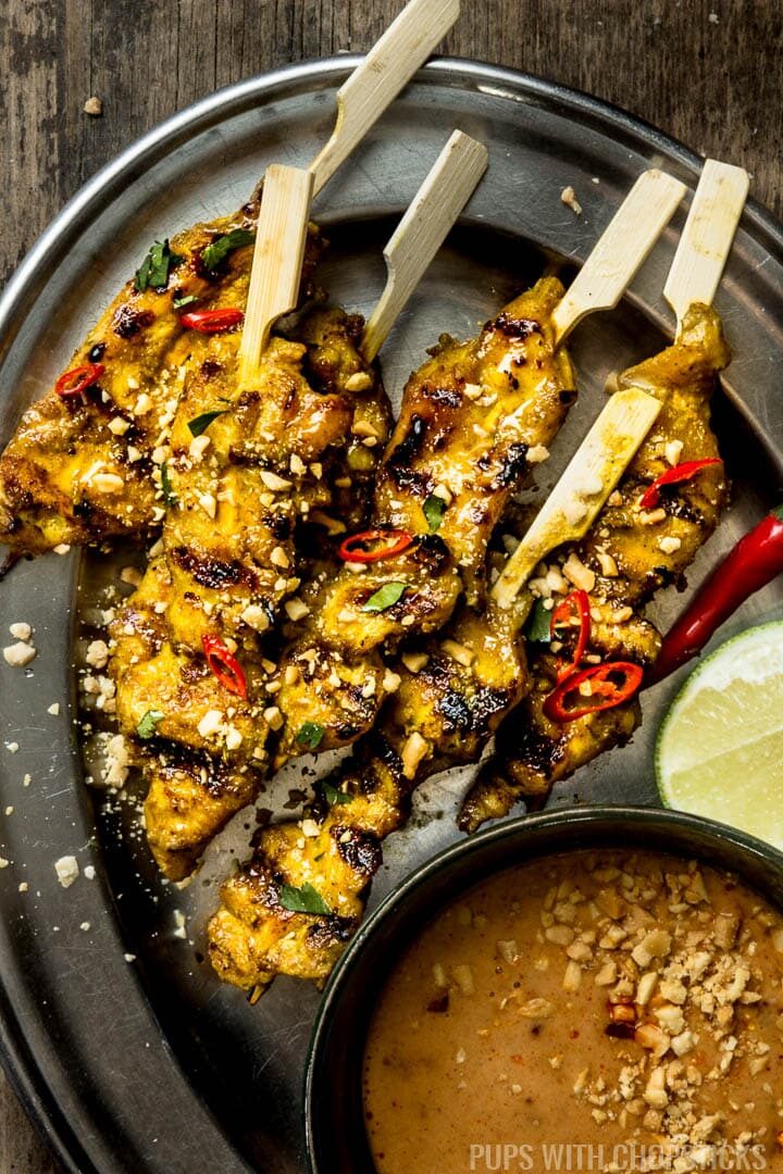 Mini Thai chicken satay skewers on a metal plate served with peanut sauce on the side with some lime wedges
