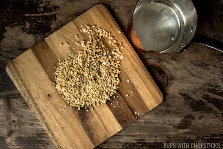 Peanuts being crushed on a cutting board with the bottom of a pot