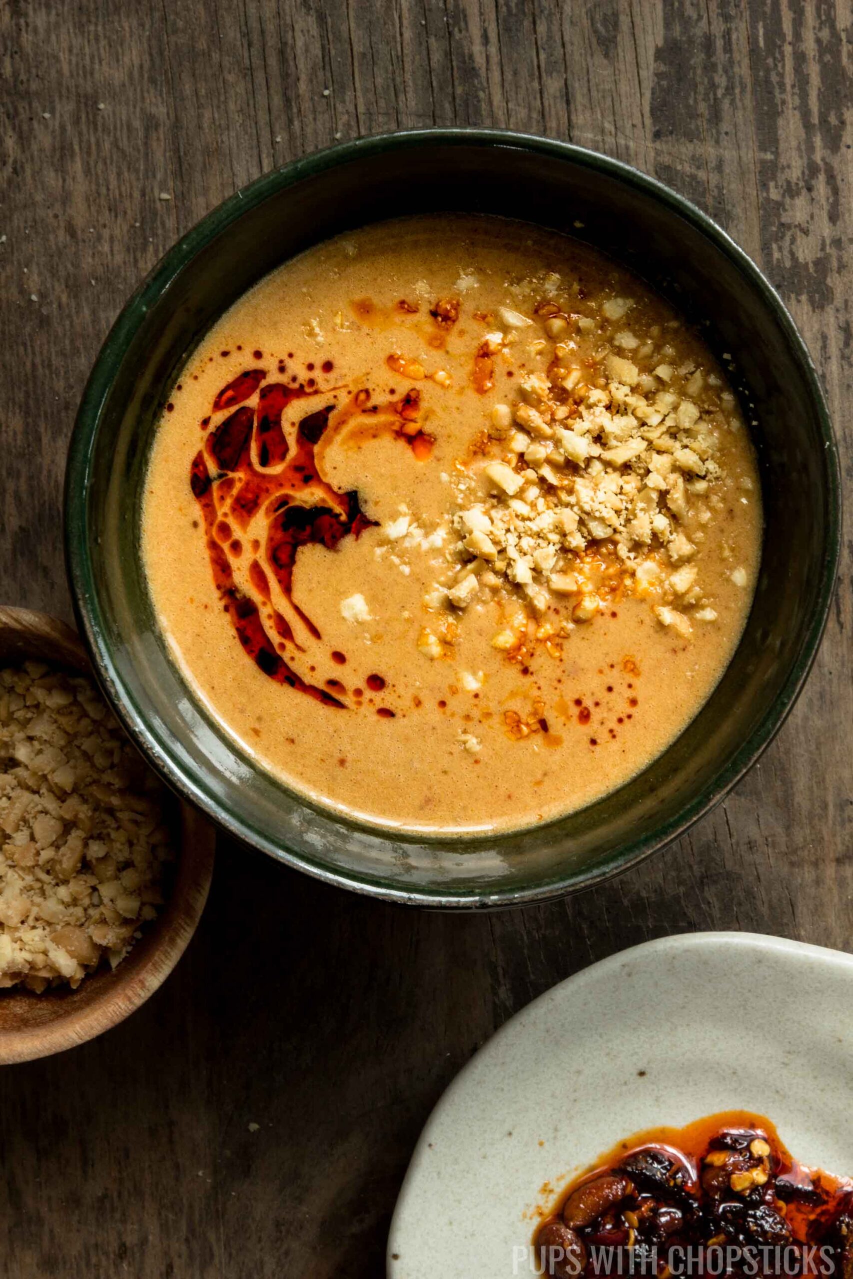 A bowl of Thai peanut sauce served with crushed peanuts on top and drizzled with chili oil